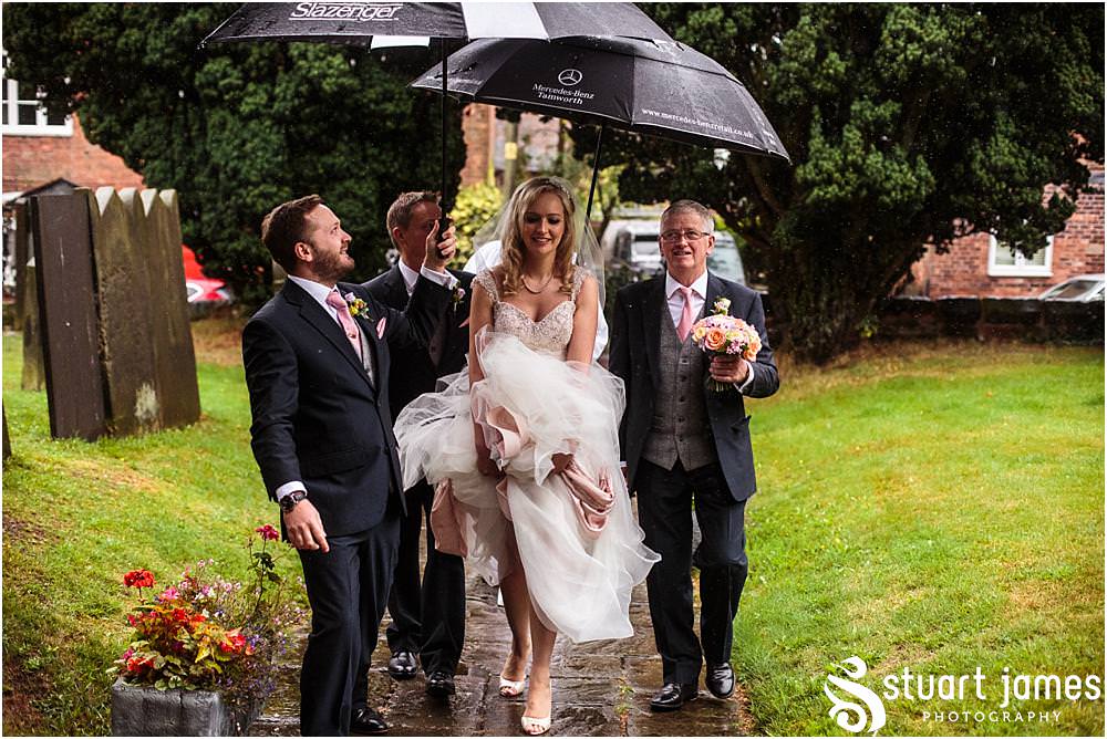 Capturing the arrival of our bride, covered with umbrellas at Middleton Church and Moxhull Hall in Sutton Coldfield by Moxhull Hall Wedding Photographers Stuart James