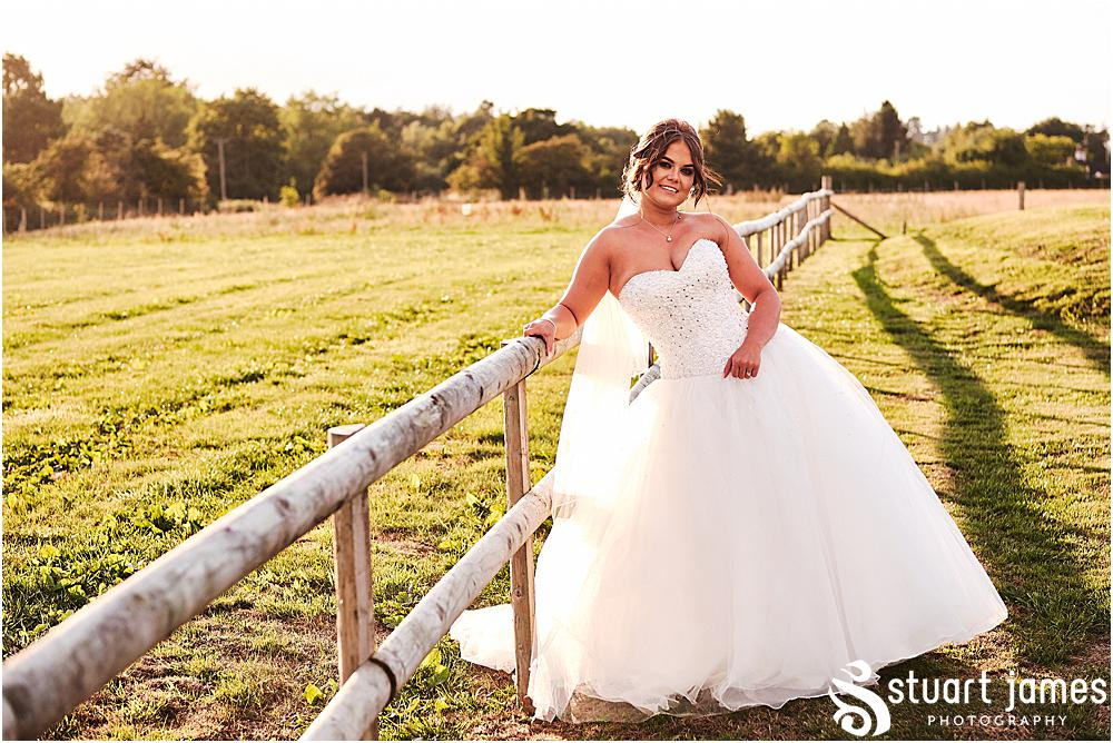 Bride posing for wedding portrait outside of wedding venue, leaning up fence in a sunny field, photo by Stuart James Photography at Aston Marina, Stone