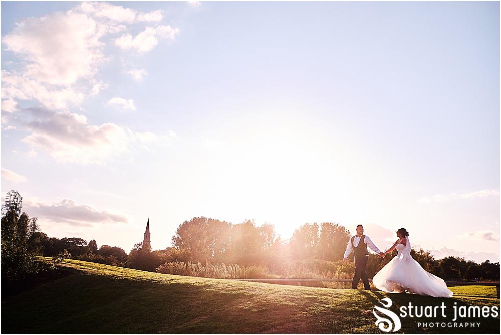 Bride and Groom walk hand in hand across the grounds of Aston Marina at Sunset with church in background, photo by Stuart James Photography at Aston Marina, Stone.