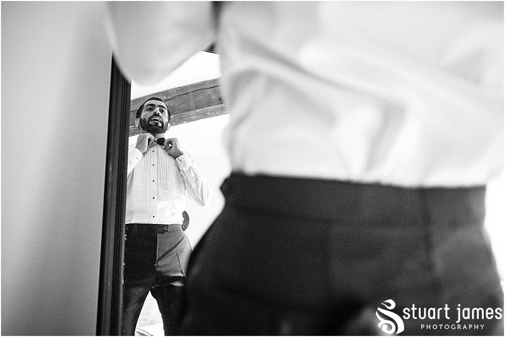 Groom adjusts bow tie in mirror whilst he dresses in his wedding suit at Davenport House in Shropshire by Davenport House Wedding Photographers Stuart James