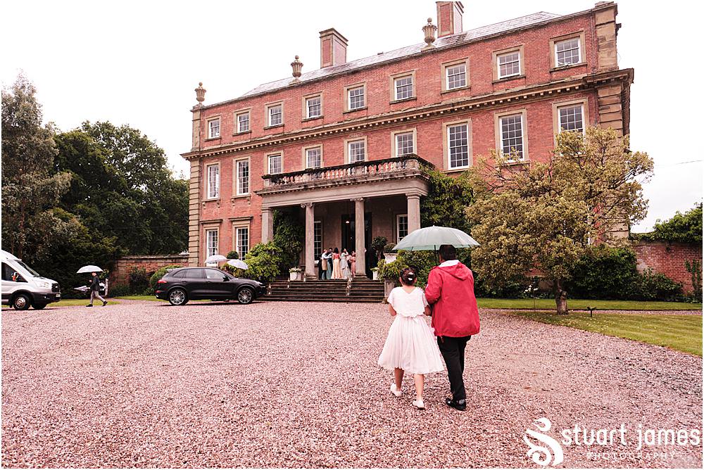 Groom and flower girl walk up driveway carrying a umbrella at Davenport House in Shropshire by Davenport House Wedding Photographers Stuart James