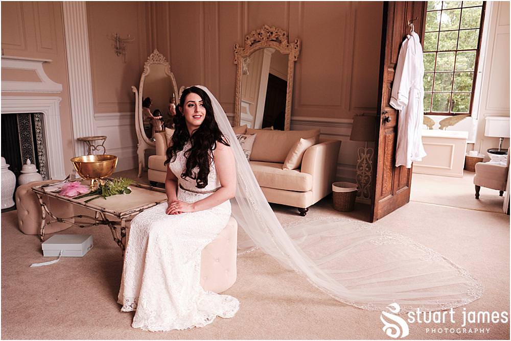 Bride poses for portrait sat down in dressing room with her lace veil trailing across the floor at Davenport House in Shropshire by Davenport House Wedding Photographers Stuart James