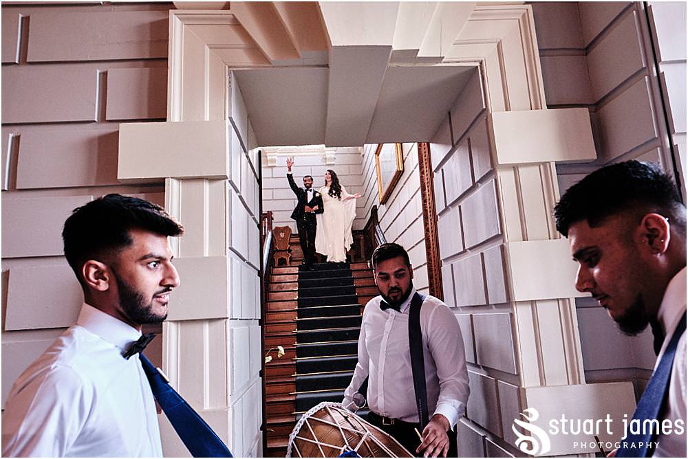 Married couple make entrance down the stairs to the sound of people playing drums at Davenport House in Shropshire by Davenport House Wedding Photographers Stuart James