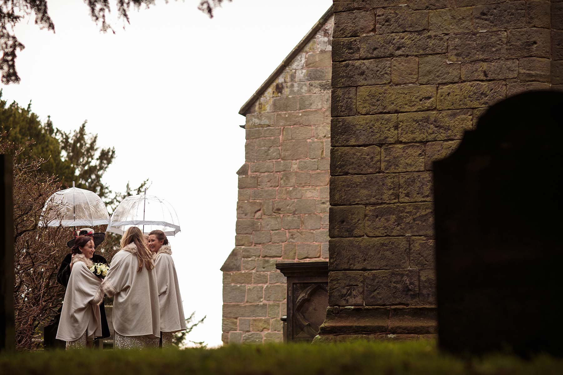 Sheltering from the rain, the bridesmaids are waiting for their bride at All Saints Church in Sandon by Stafford Recommended Wedding Photographer Stuart James