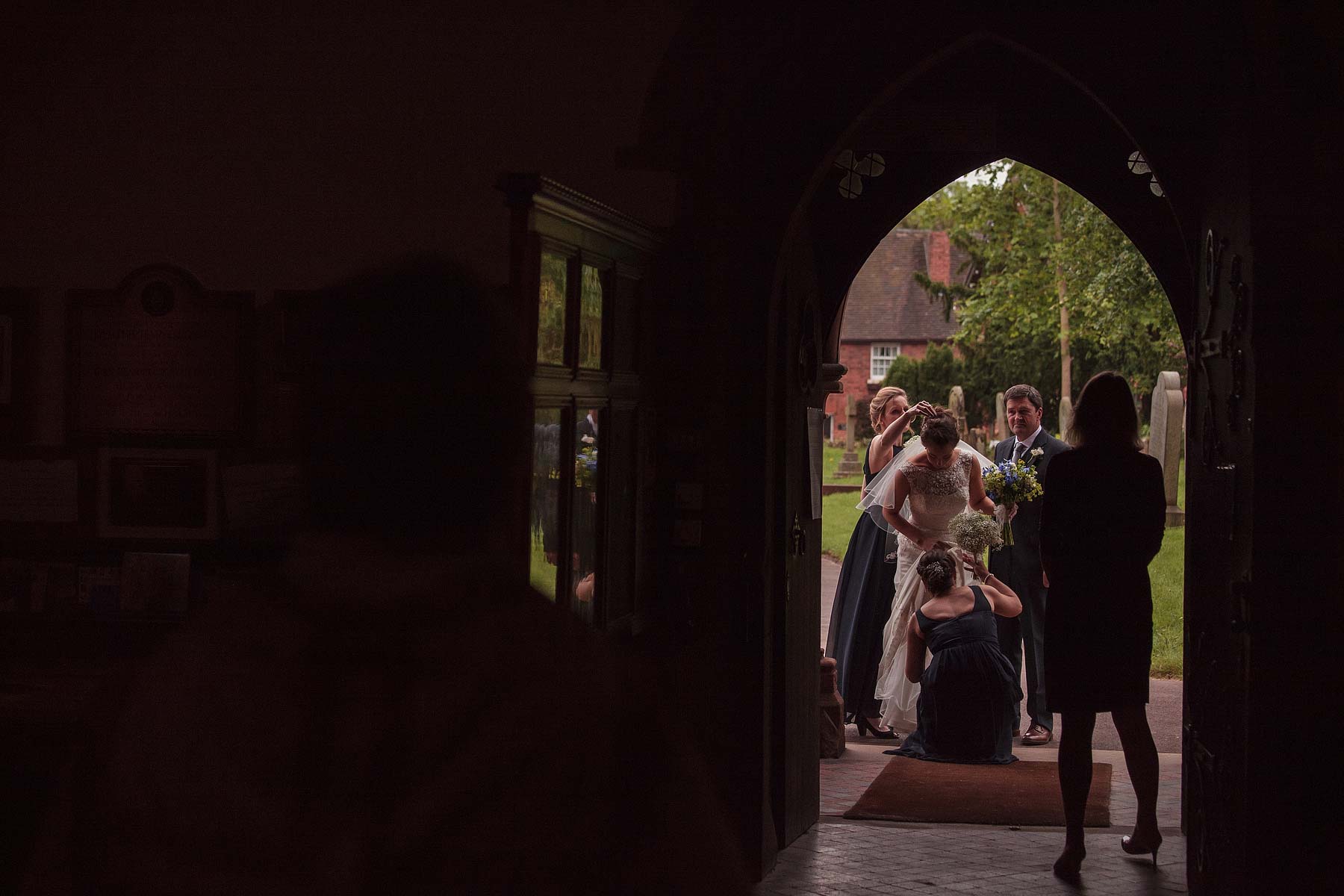 Finishing touches as the bride is attended by her bridesmaids in the doorway to St Chads Church in Pattingham by Pattingham Wedding Photographer Stuart James