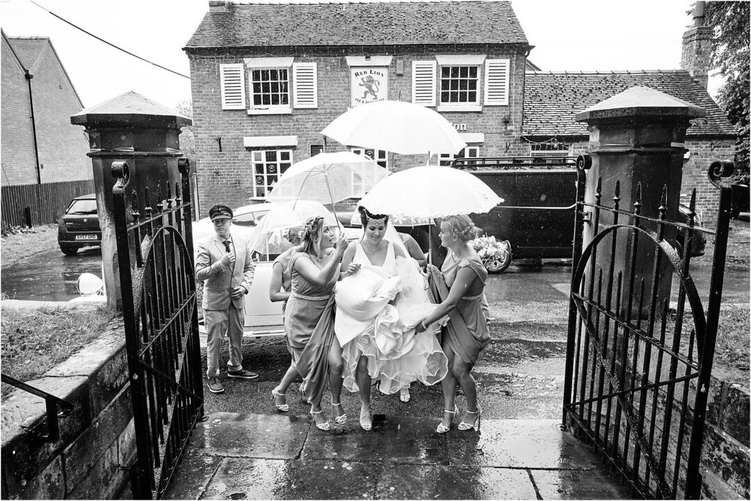 Documenting storytelling memories with the Bride arriving in the rain at the Church for the wedding at Heath House in Staffordshire by Documentary Wedding Photographer Stuart James